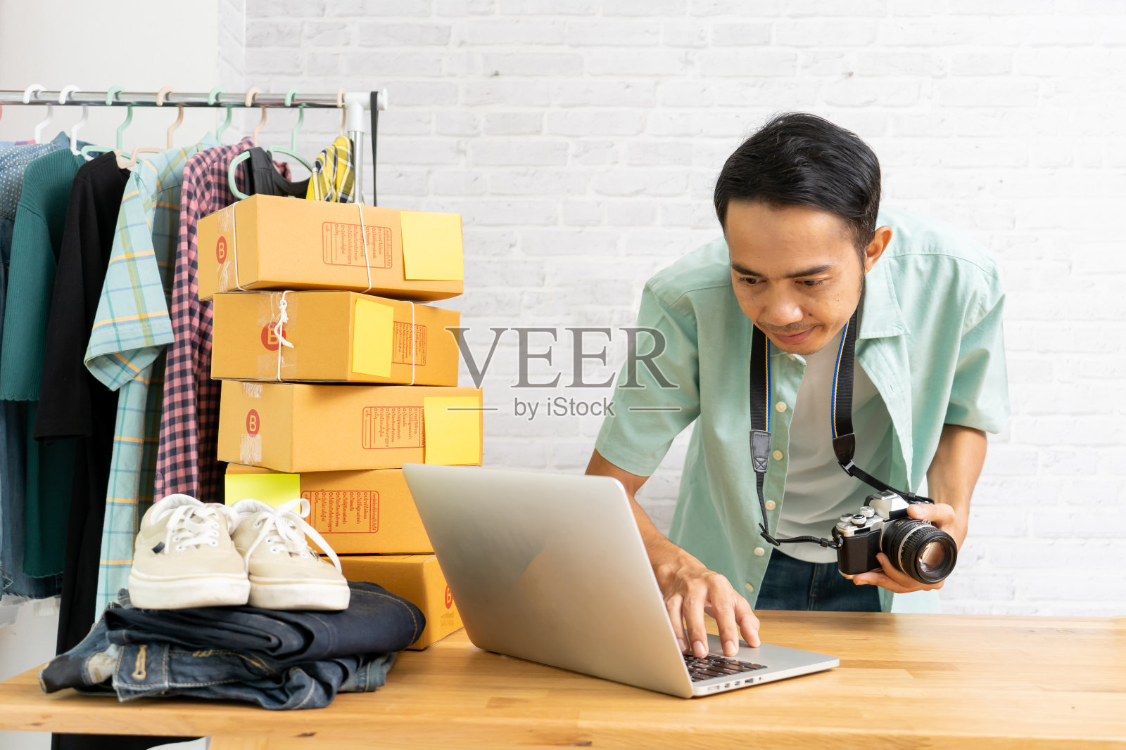 亚洲人工作笔记本电脑销售网上创业小企业主,与持有相机准备采取产品的电子商务理念照片摄影